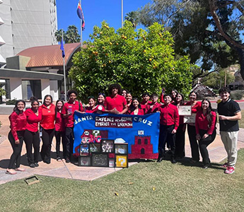 Group photo of students dressed in red and black holding a Santa Cruz banner outside